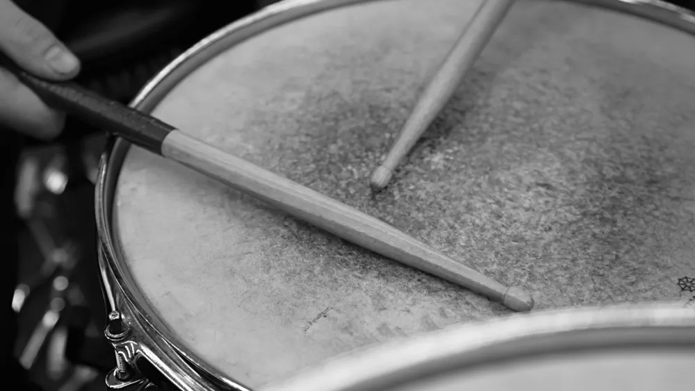 Pair of drumsticks resting on a snare drum, grayscale