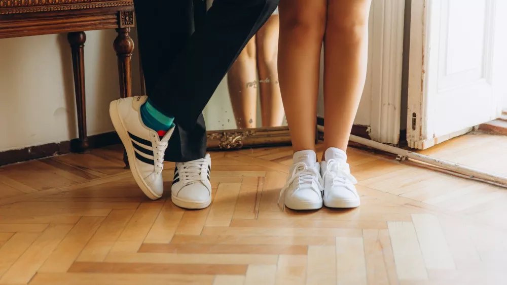Close-up of a couple's feet in white sneakers on a wooden floor