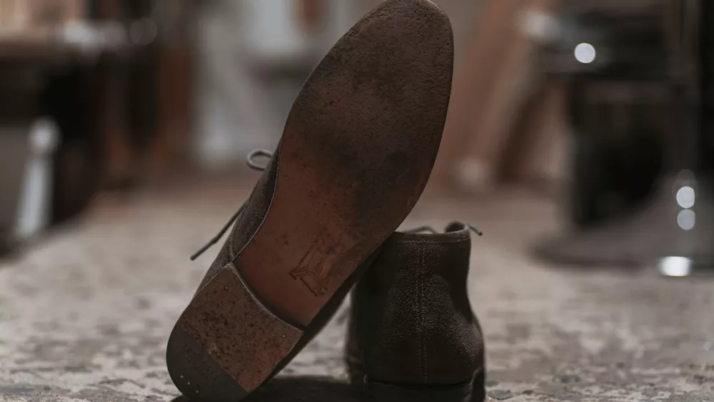 A worn brown leather shoe sole, scuffed at the ball of the foot, leaning against its pair