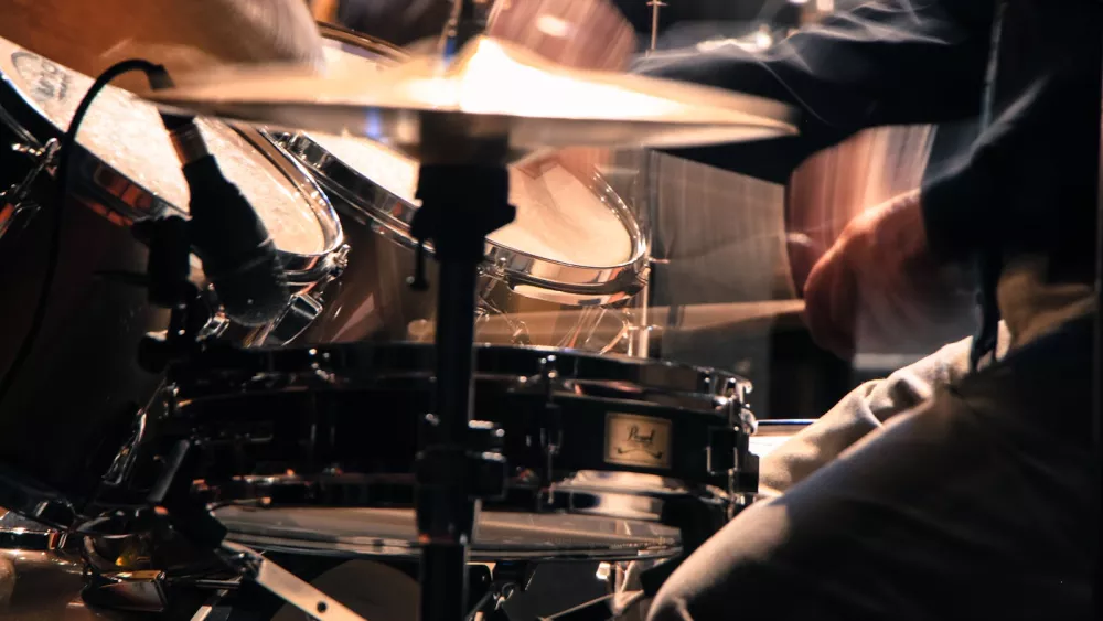 Drummer playing energetically at a concert, sticks mid-strike above the snare