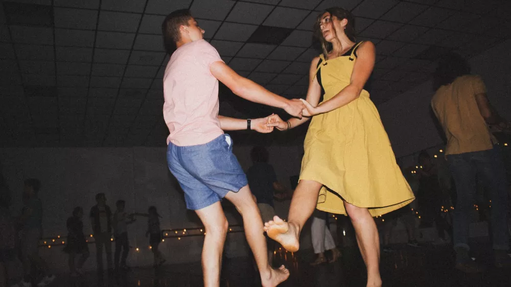 Two dancers mid-swingout in a hall, in jeans and a t-shirt, with fairy lights along the back wall